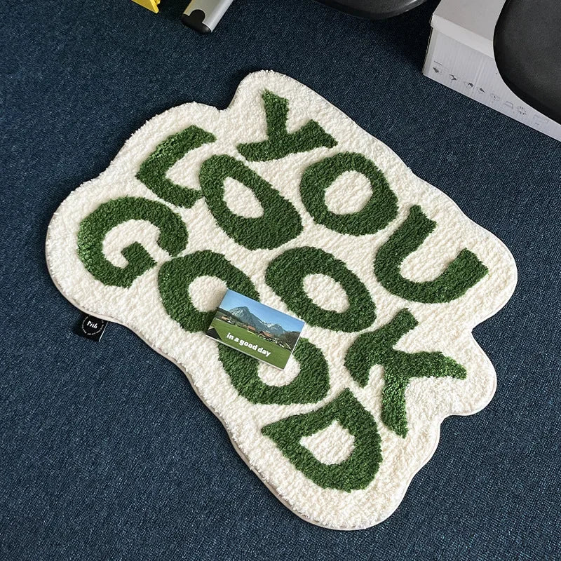 A white foot mat with green embossed text that reads 'GOOD YOU GOOD' is placed on a dark blue surface.