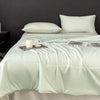 A light mint green lightweight cooling blanket is displayed on a bed with white pillows and a candle.
