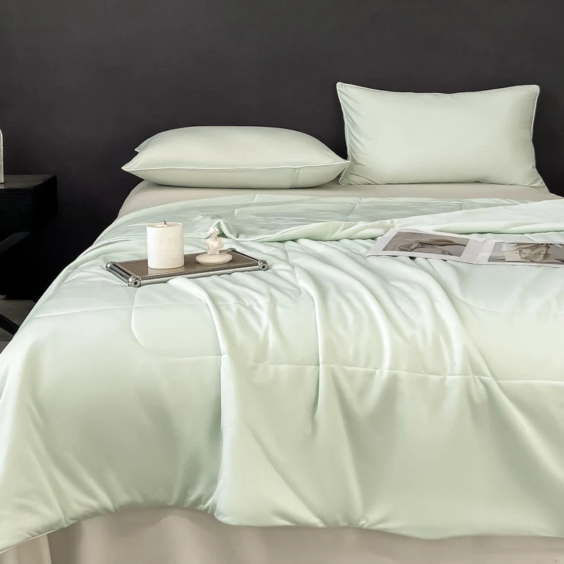 A light mint green lightweight cooling blanket is displayed on a bed with white pillows and a candle.