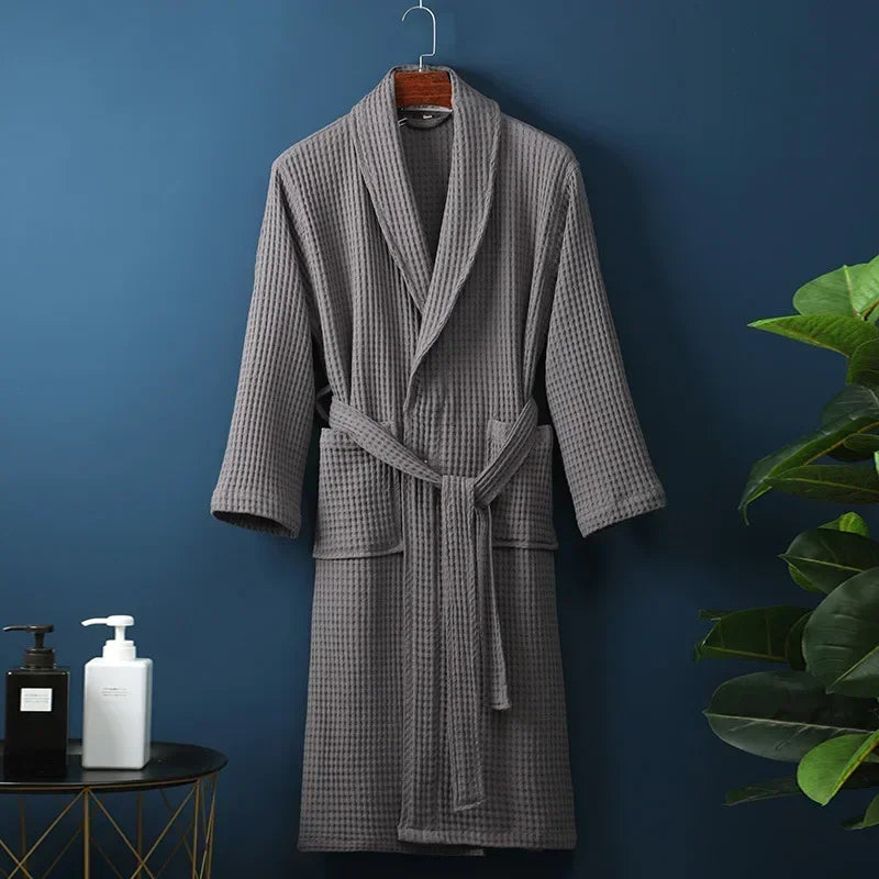 A long, gray cotton terry robe hanging on a dark blue wall next to a potted green plant.