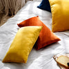 A collection of velvet throw pillows in shades of mustard yellow, orange, and deep rust resting on a white textured blanket.