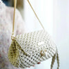 A light beige knitted pouch made from thick craft yarn is being held against a blurred background.