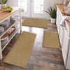 A row of natural fiber kitchen runner mats in beige and olive green rests on a dark wood floor near white cabinetry.