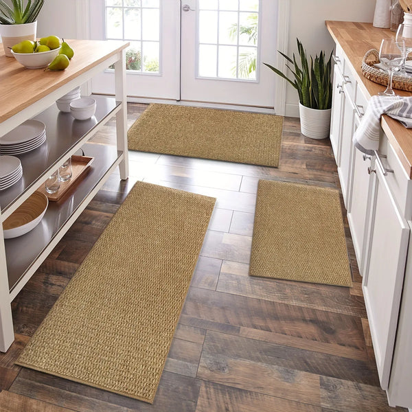 A row of natural fiber kitchen runner mats in beige and olive green rests on a dark wood floor near white cabinetry.