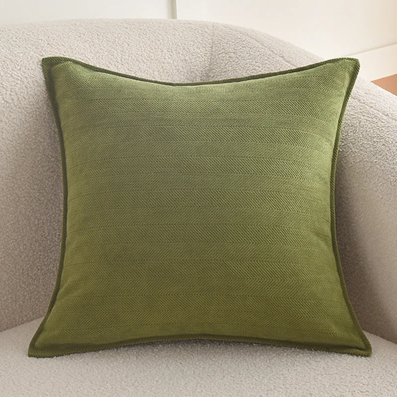 A square olive green chenille throw pillow resting on a light beige textured sofa.