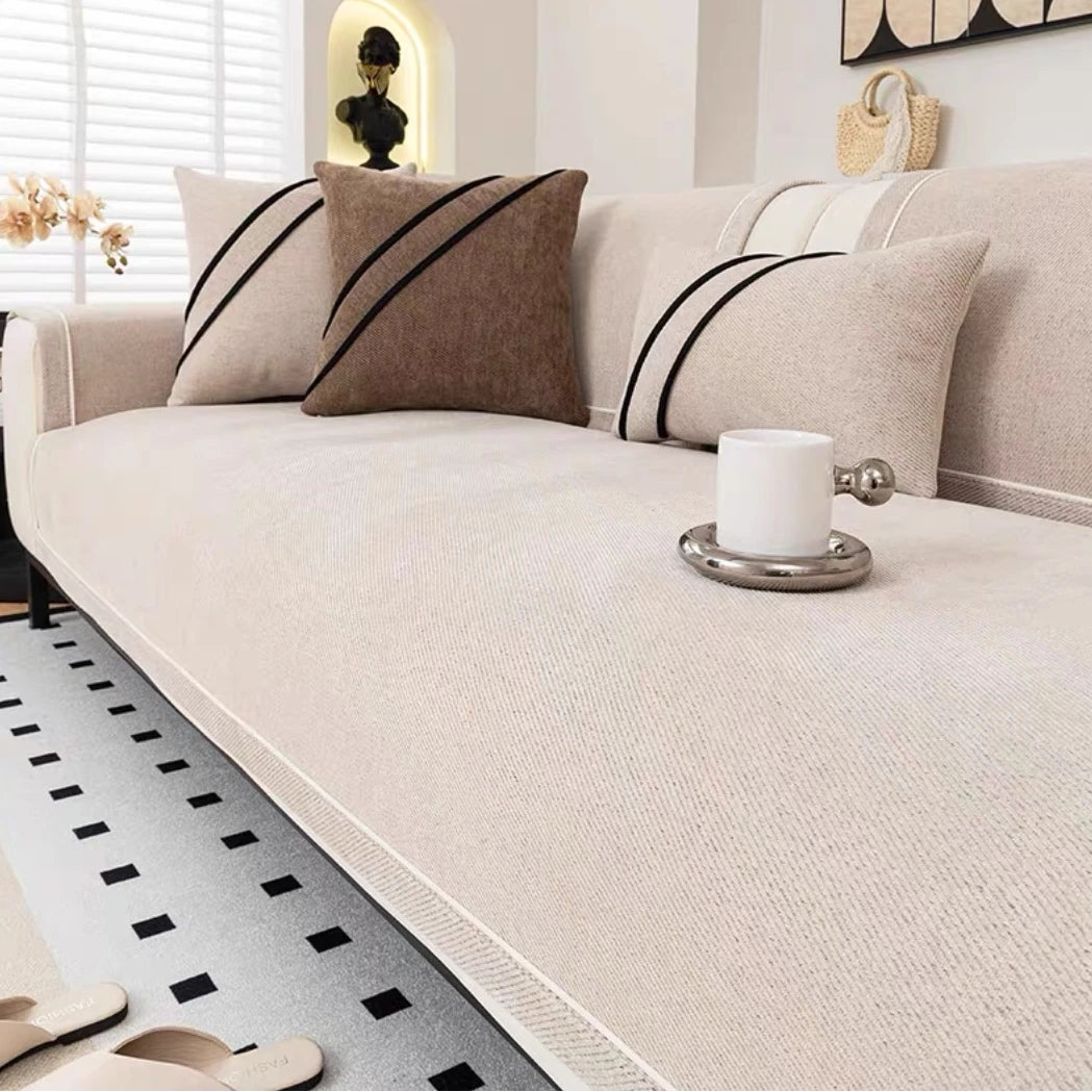 A light beige chenille sofa protector cover with black striped accent pillows and a white mug on the surface.
