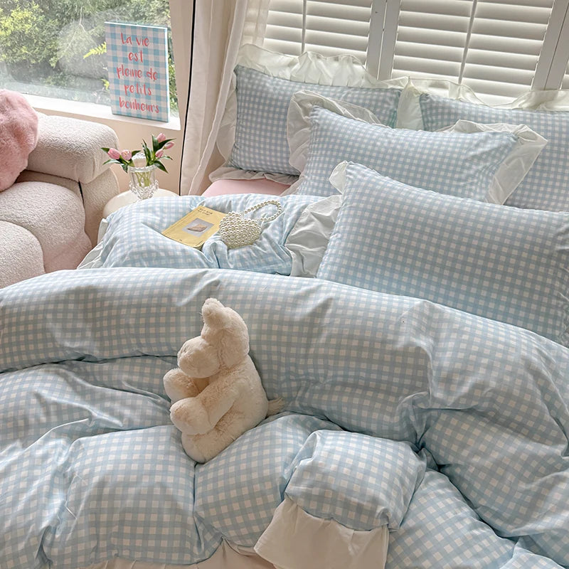 A light blue and white gingham duvet cover set with pillows and a stuffed bear on a bed.