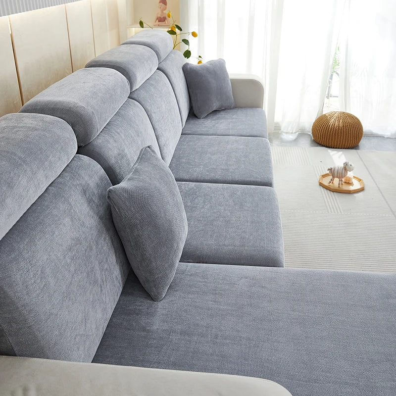 A light gray stretchable chenille sofa cushion cover on a sectional sofa with white trim and natural light.