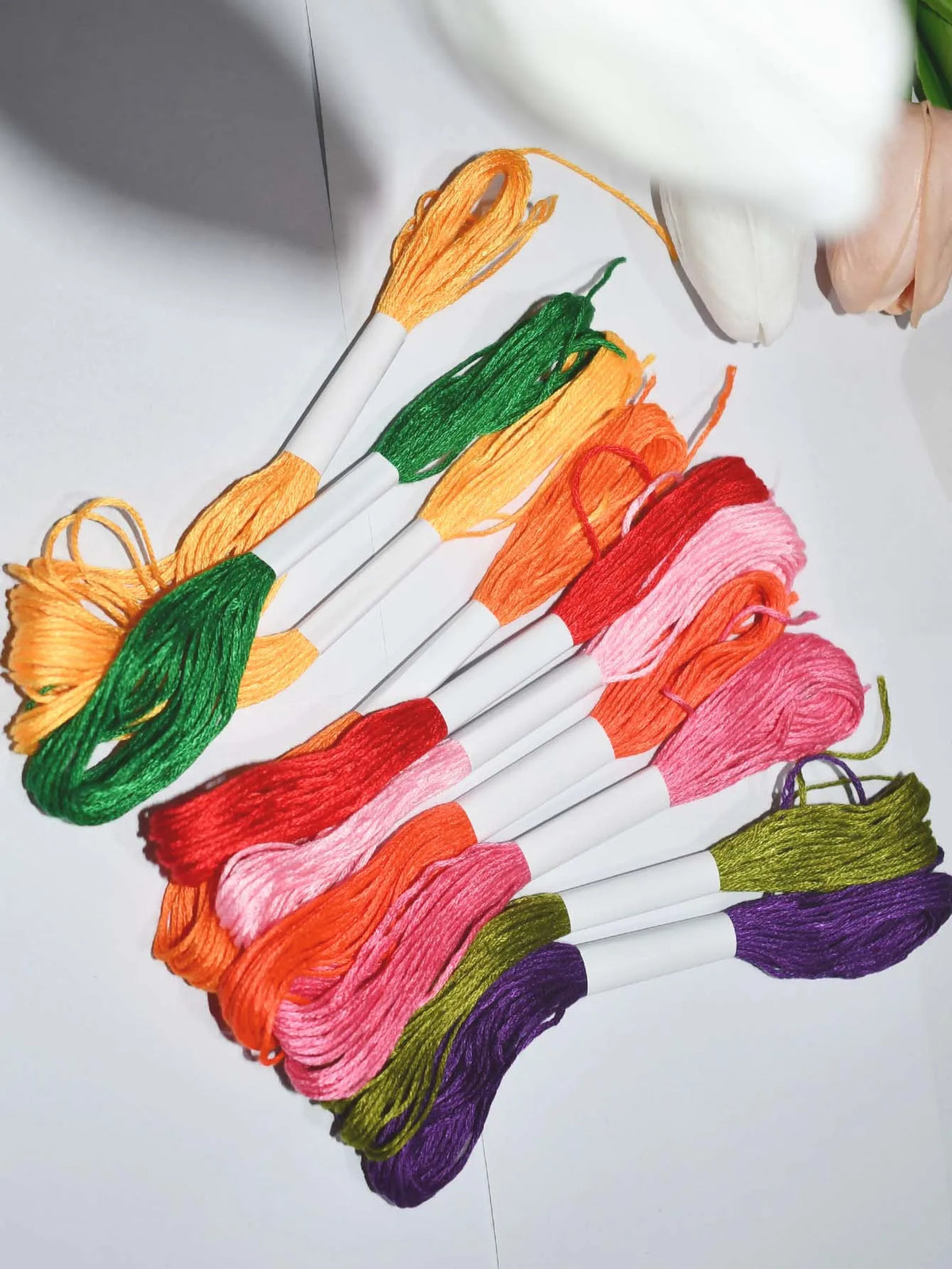 A collection of vibrant 250-color polyester cross-stitch threads in various shades of orange, green, pink, and purple arrange
