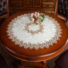 A round wooden table set with an elegant lace-trimmed white tablecloth and a floral centerpiece.