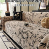 A beige chenille sofa slipcover featuring a black floral and bird pattern, displayed indoors.