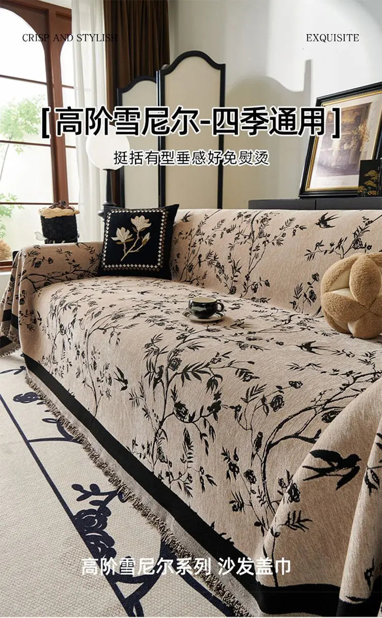 A beige chenille sofa slipcover featuring a black floral and bird pattern, displayed indoors.
