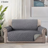 A gray slip-on protective sofa cover for a two-seater armchair with beige trim and quilted fabric.