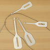 A collection of stainless steel needle threaders and tweezers laid out on a wooden surface.