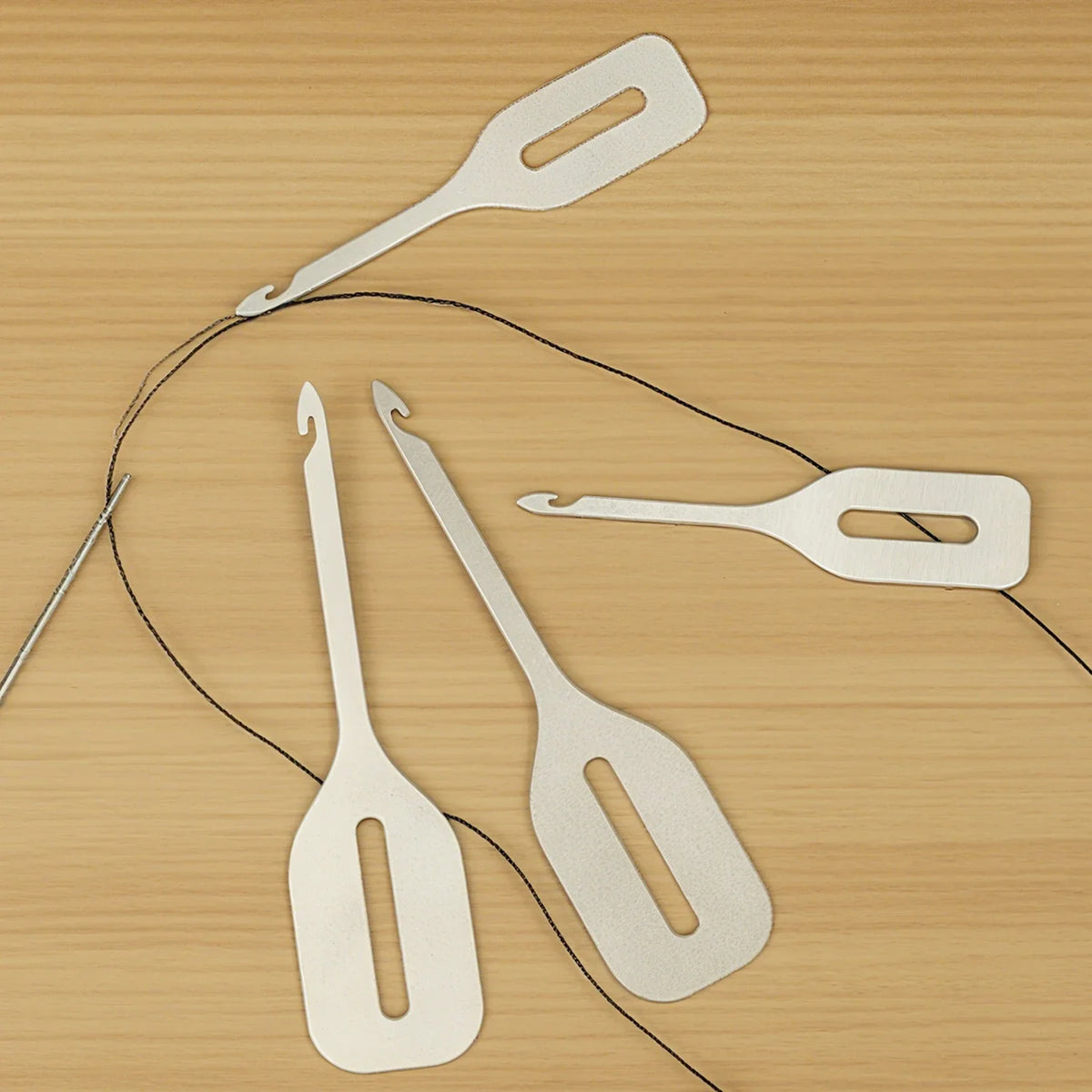 A collection of stainless steel needle threaders and tweezers laid out on a wooden surface.
