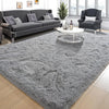 A gray shaggy rug is placed on a wooden floor in a living room setting with a sofa and armchair.
