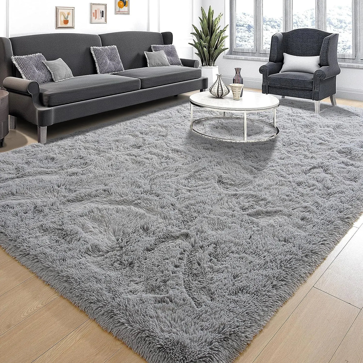 A gray shaggy rug is placed on a wooden floor in a living room setting with a sofa and armchair.