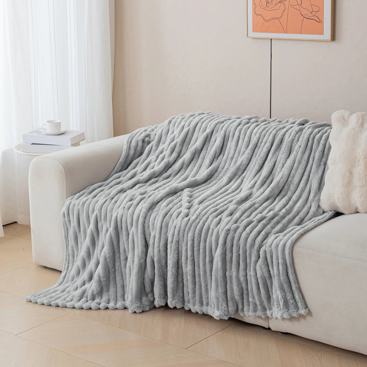 A soft gray flannel throw blanket draped over a light-colored sofa in a bright room.
