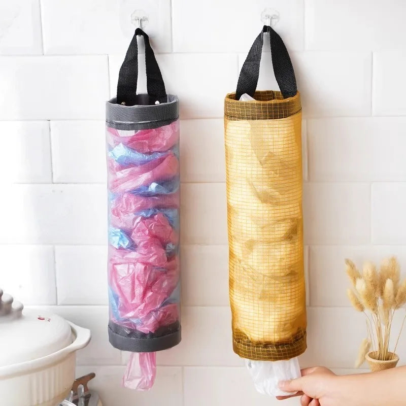 A vertical hanging mesh trash bag in pink and blue is displayed against a white tiled wall.