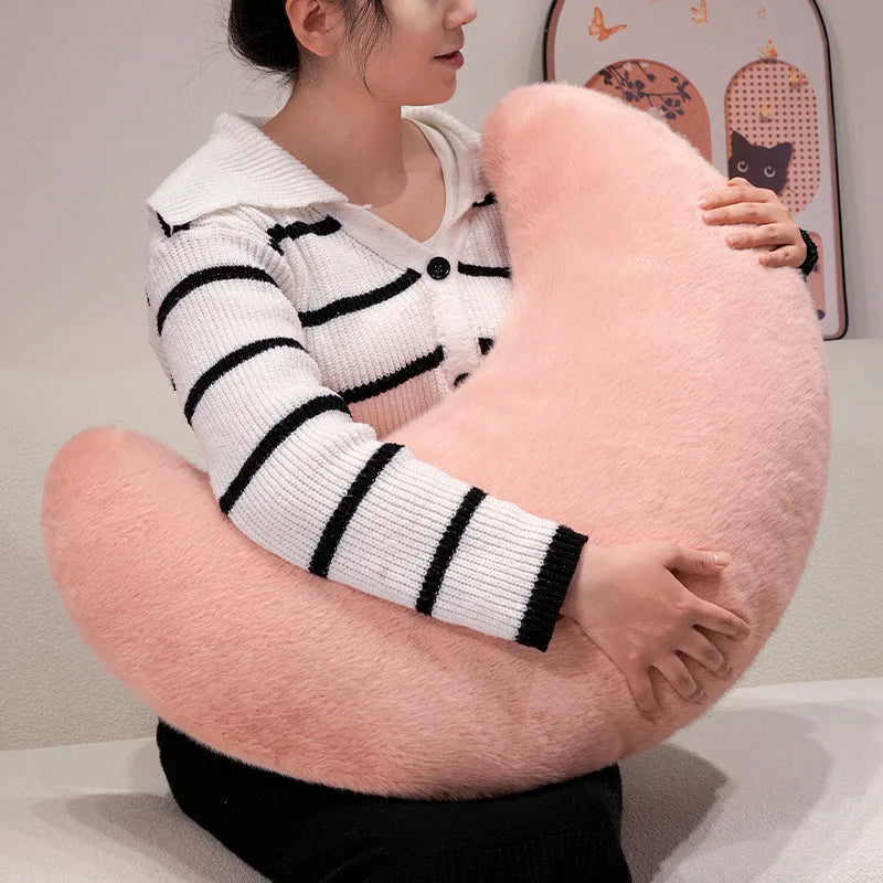 A woman is holding a large, pink moon-shaped throw pillow with black and white striped knit sweater.