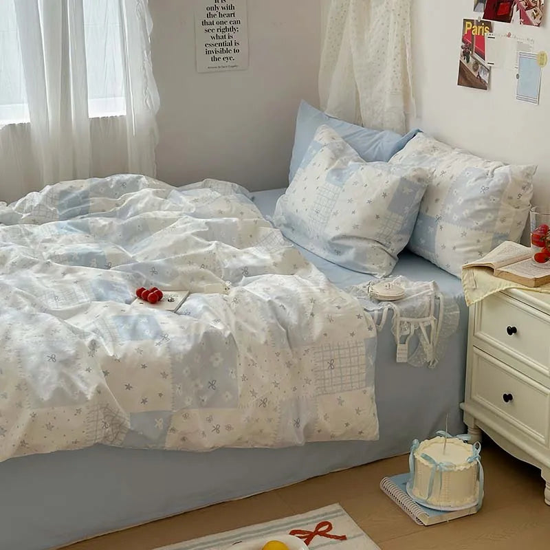 A bed with a light blue duvet cover, white floral patterns, and blue pillows in a bright room.