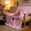 A pink and white striped throw blanket featuring a C-Curious George design draped over a wooden chair.