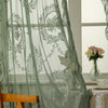 Sheer sage green lace curtains with floral patterns hanging in a bright window.