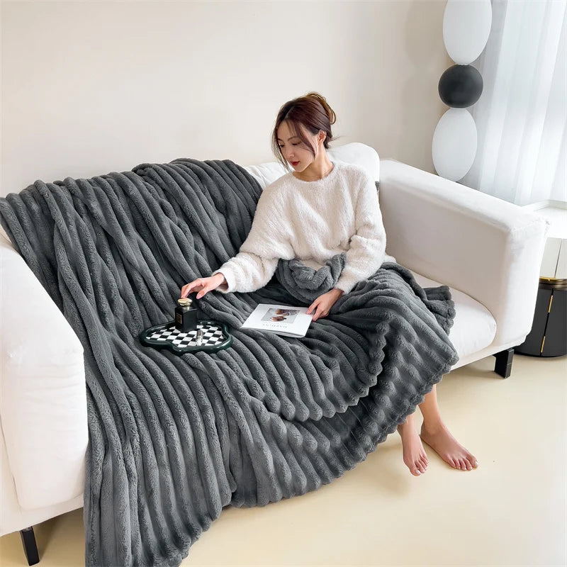A woman is sitting on a white sofa wrapped in a gray ultra-soft plush winter blanket.