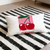 A white cushion cover featuring a pink cherry design with the text Happy.