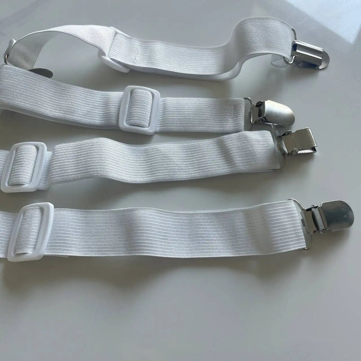 White adjustable bed sheet grippers and fasteners laid out on a white surface.