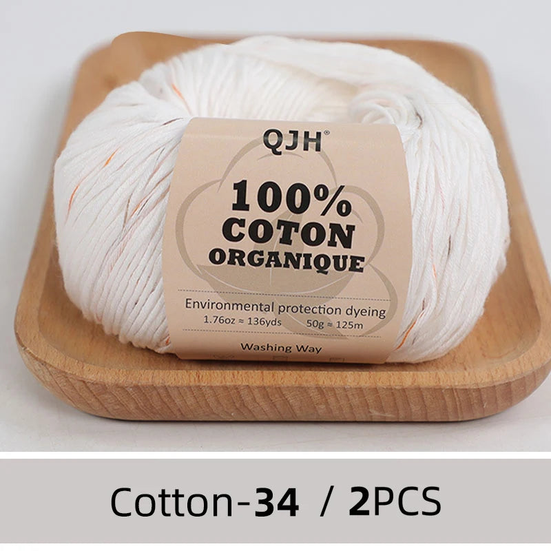 A ball of white organic cotton yarn labeled QJH 100% COTON ORGANIQUE resting on a wooden tray.