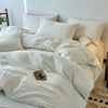 A white cotton yarn-dyed duvet cover with several pillows and a small wooden object on a bed.