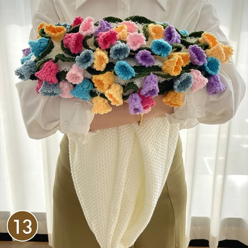 A hand knitted floral rose bouquet arrangement featuring colorful yarn flowers and a cream colored throw blanket.