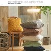 A stack of various textured cushions in yellow, gray, beige, and green on a wooden surface.