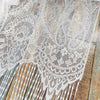 Close-up of vintage lace tassel door curtains featuring intricate white and beige floral patterns against a weathered wooden 
