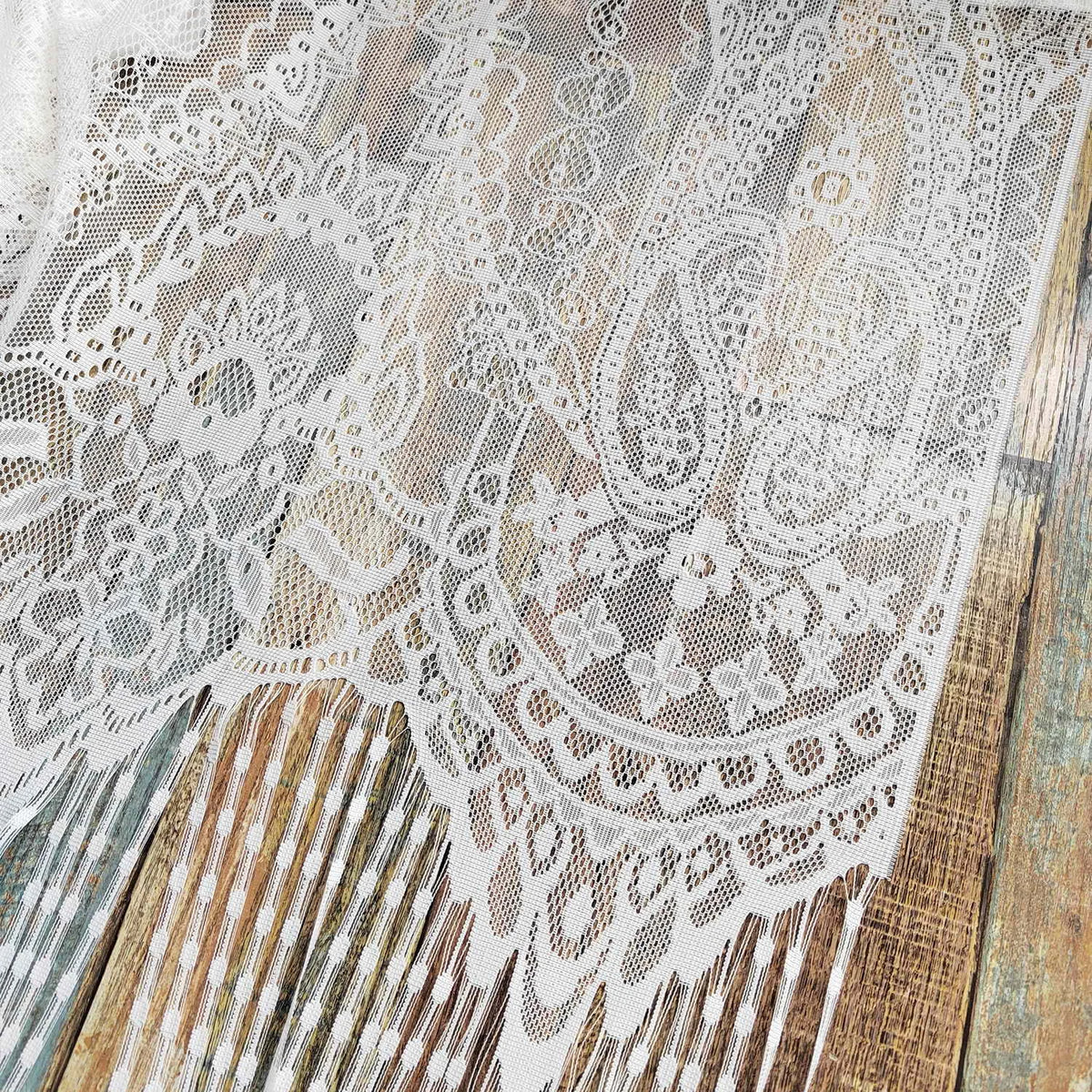 Close-up of vintage lace tassel door curtains featuring intricate white and beige floral patterns against a weathered wooden 