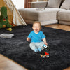A toddler sits on a black plush living room rug with toy cars and a green stuffed dinosaur in the background.