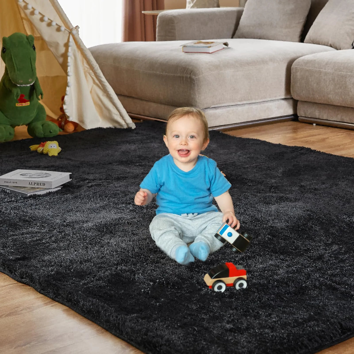 A toddler sits on a black plush living room rug with toy cars and a green stuffed dinosaur in the background.