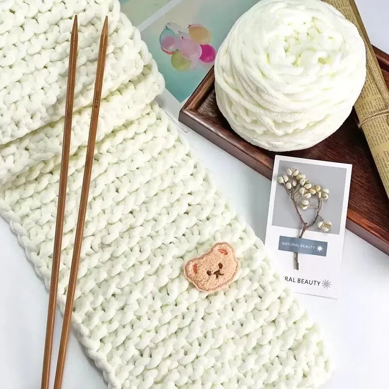 A ball of white chenille knitting yarn next to wooden knitting needles and a small card.