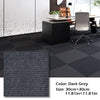 Dark grey square carpet tiles displayed on a floor with modern office furniture and a white wall.