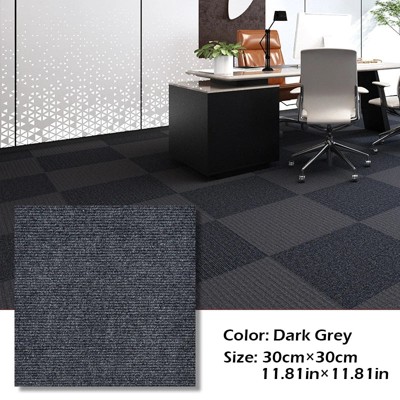 Dark grey square carpet tiles displayed on a floor with modern office furniture and a white wall.