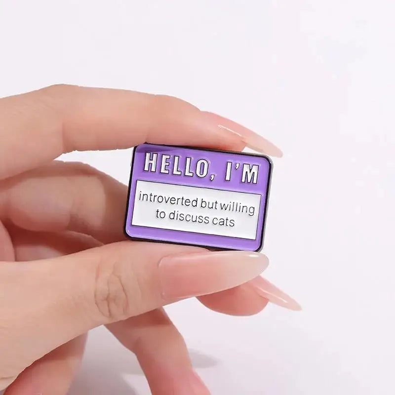 A purple enamel lapel pin with the text Hello I'm introverted but willing to discuss cats