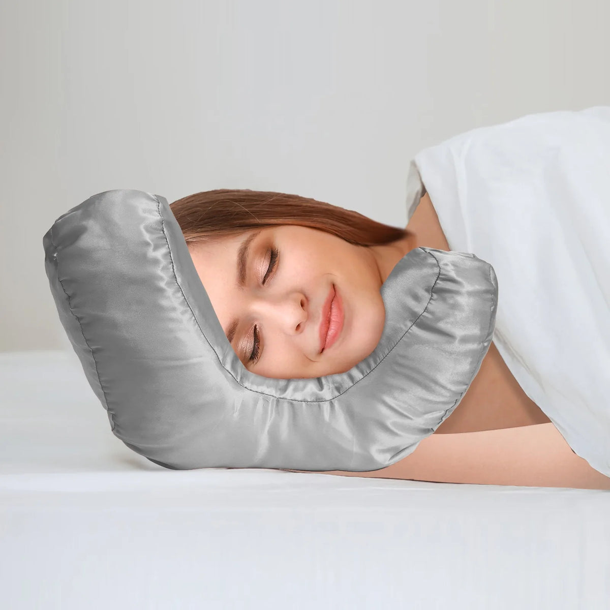 A woman is resting her face on a gray satin anti-wrinkle pillow for beauty and sleep.