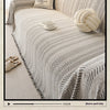 A close-up of a light beige sofa cover featuring an elegant fishbone pattern, with a white knitted ball and a teacup resting 