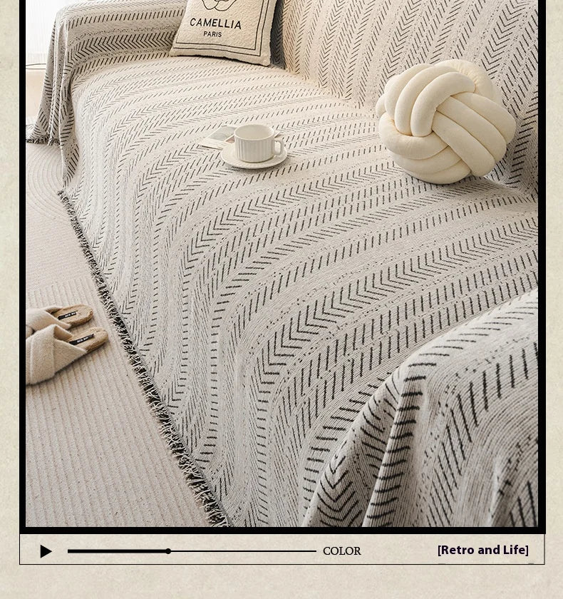 A close-up of a light beige sofa cover featuring an elegant fishbone pattern, with a white knitted ball and a teacup resting 