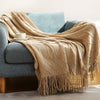 A beige knitted tassel throw blanket draped over a blue armchair.