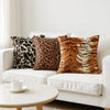 Two leopard print throw pillow covers on a white sofa with a round table nearby.