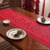 A red lace table runner with intricate patterns and tassels is displayed on a wooden table.