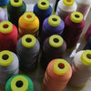 A collection of spools of high tenacity polyester sewing thread in various colors including green, black, purple, orange, and