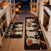 A set of black non-slip kitchen rugs featuring Halloween ghost and pumpkin prints placed on a wooden floor.